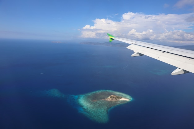 Avión volando sobre el mar azul profundo con una foto de la isla a través del avión de la ventana