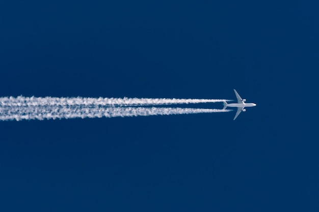 El avión vuela dejando un rastro de estela en un cielo azul alto y claro.