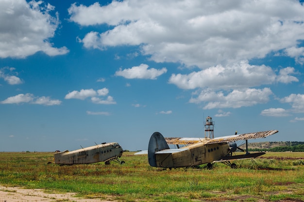 Aviones viejos abandonados, destruidos y oxidados se paran en la hierba bajo un cielo azul con nubes blancas.