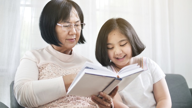 Avó asiática feliz e linda menina lendo livro juntos em casa