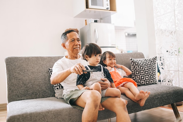 Avô asiático assistindo televisão junto com netos na sala de estar