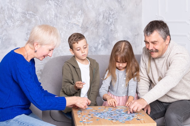 Avó, avô e neta colecionam quebra-cabeças à mesa na sala de estar. A família passa tempo juntos, jogando