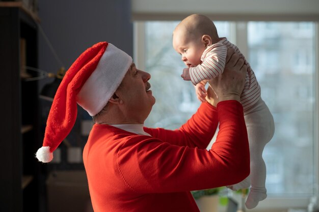 Avô caucasiano de chapéu vermelho brincando com a neta em casa celebrando o Natal