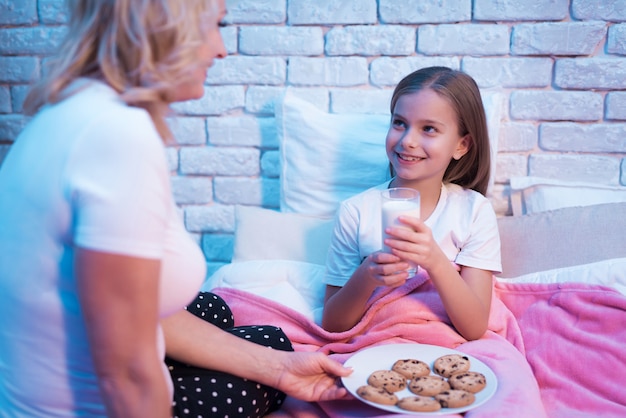 Avó com bolinhos de menina e leite na cama