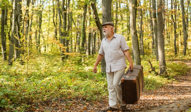 Avô com mala vintage na natureza unidos com a natureza fim de semana na natureza homem maduro com barba branca na floresta hobby e lazer pessoas idosas férias e relaxar conceito de aposentadoria