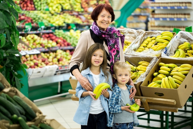 avó com netos escolher legumes e frutas em um grande supermercado.