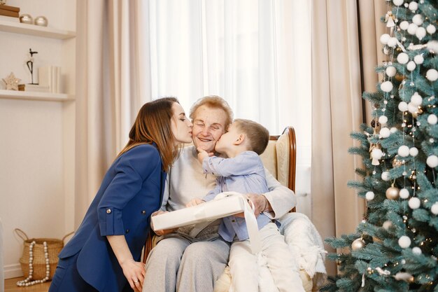 Avó com sua filha e neto sentado perto da árvore de Natal