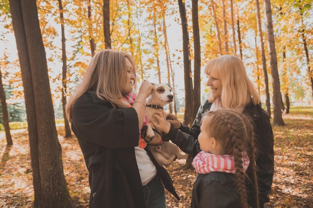 Avó e mãe com a neta se divertindo com o cachorro no lazer de geração da temporada de outono