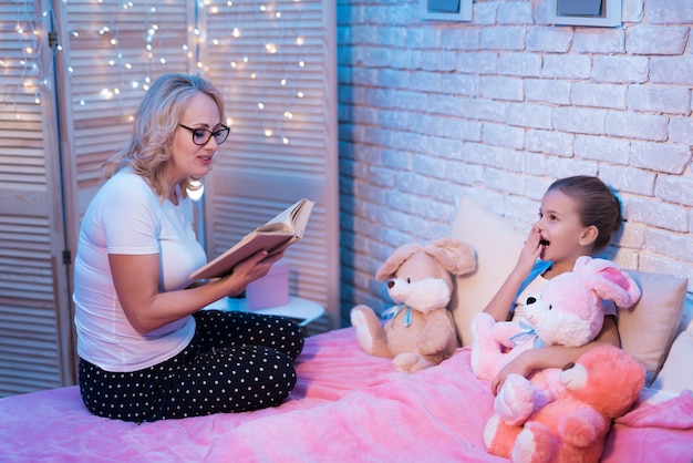 Avó e neta estão lendo livro infantil à noite em casa