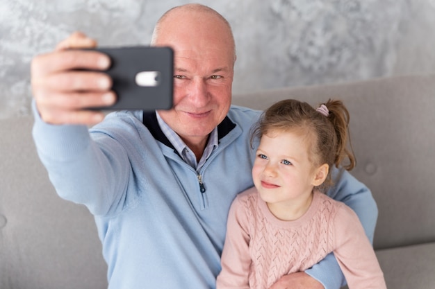 Avô e neta sentada no sofá e tomando selfie