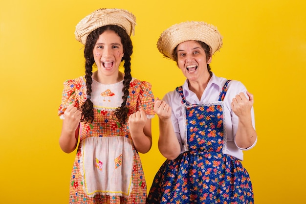 Avó e neta vestidas com roupas típicas da Festa Junina Chamando com as mãos convidando venha aqui