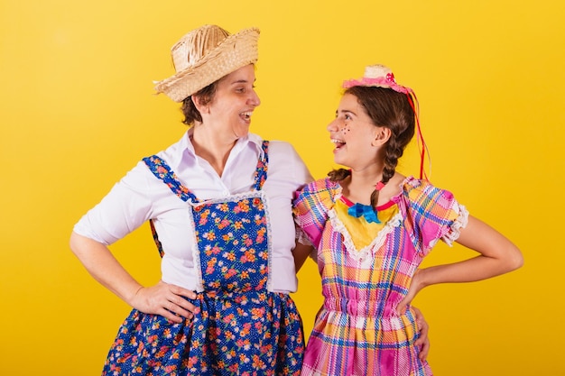 Avó e neta vestidas com roupas típicas da Festa Junina Mãos nos quadris sorrindo