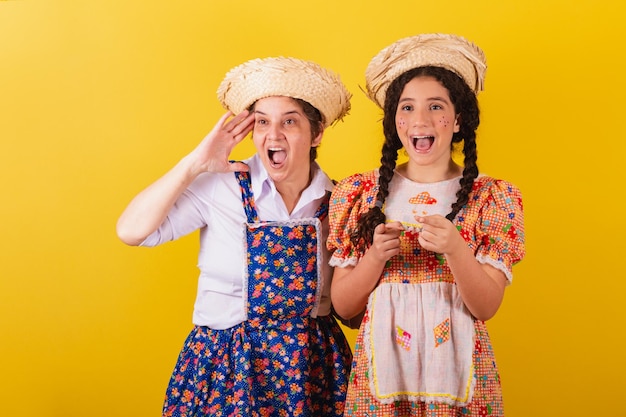 Avó e neta vestidas com roupas típicas da Festa Junina Olhando e vendo algo ao longe