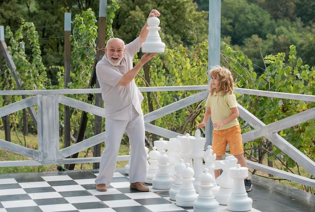 Avô e neto jogando xadrez no grande tabuleiro de xadrez idoso parente velho com criança
