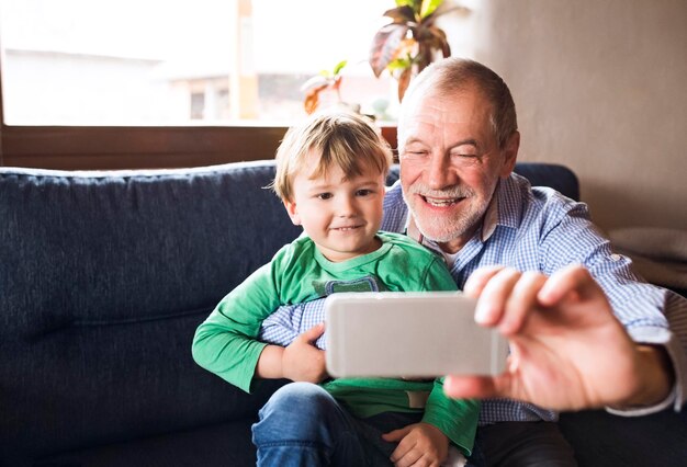 Avô e neto sentados no sofá, tirando selfies de smartphone