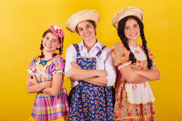 Avó e suas duas netas vestidas com roupas típicas da Festa Junina Braços cruzados sorrindo felizes