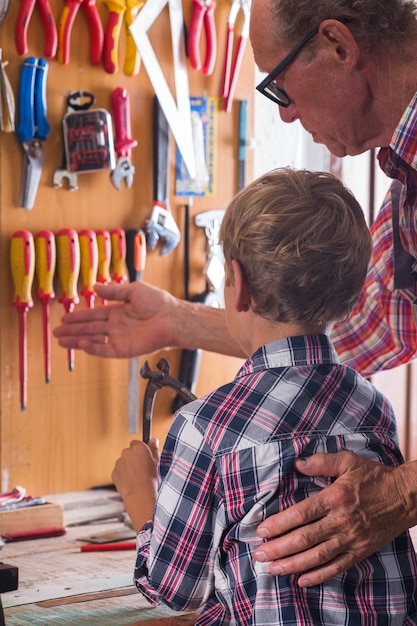 Avô ensina menino a trabalhar na bancada com ferramentas de marcenaria