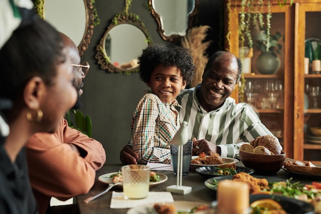 Avô feliz africano sentado à mesa com o neto de joelhos e rindo durante a conversa