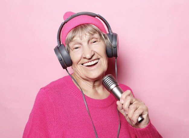 Avó feliz com fones de ouvido e microfone sobre fundo rosa