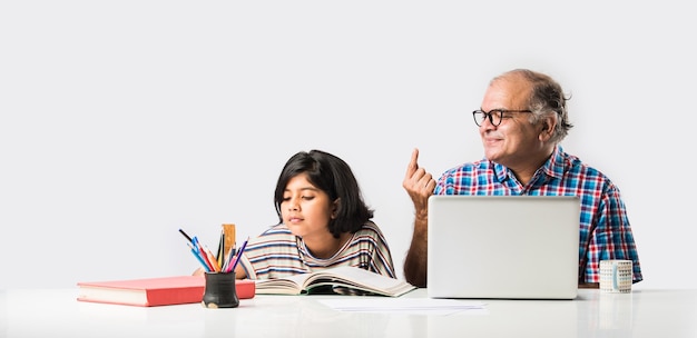 Avô indiano ensinando neta com livros, lápis e laptop, ensino doméstico ou aulas