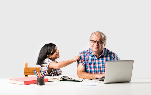 Avô indiano ensinando neta com livros, lápis e laptop, ensino doméstico ou aulas