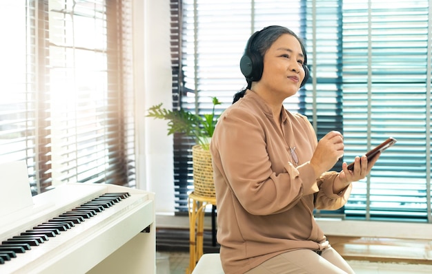 Avó ouve música antiga no fone de ouvido perto do piano Mulher asiática idosa idosa gosta de relaxar com o fone de ouvido sem fio de música que toca músicas antigas como pensa nos velhos tempos e lembra-se do espaço de cópia da pessoa legal