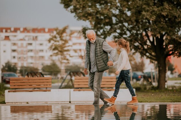 Avô passando tempo com sua neta por uma pequena piscina de água no parque no dia do outono