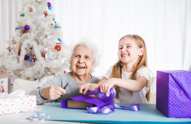 Avó sorridente com a netinha decorando presentes juntas no Natal