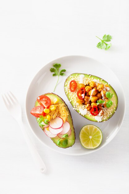 Avocado-Boote gefüllt mit Hummus, Tomaten, Radieschen, gerösteten Kichererbsen