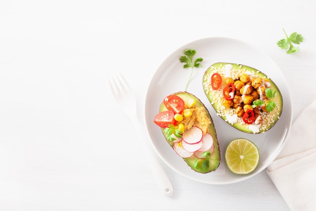 Avocado-Boote gefüllt mit Hummus, Tomaten, Radieschen, gerösteten Kichererbsen