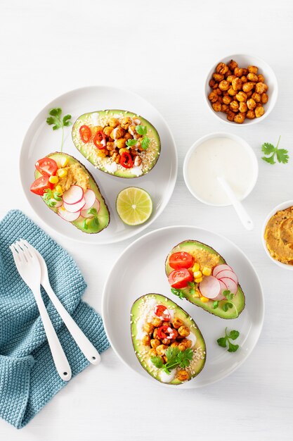 Avocado-Boote gefüllt mit Hummus, Tomaten, Radieschen, gerösteten Kichererbsen