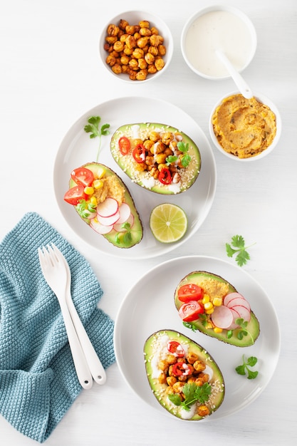 Avocado-Boote gefüllt mit Hummus, Tomaten, Radieschen, gerösteten Kichererbsen