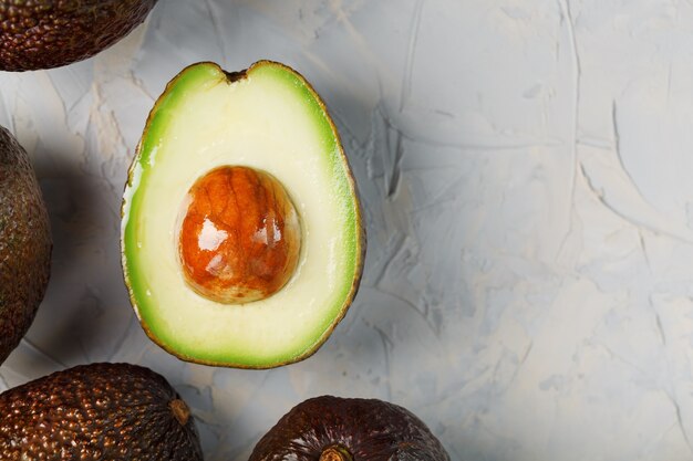 Avocado-Hälften mit ganzen Hass-Früchten auf einer Oberfläche aus grauem Beton