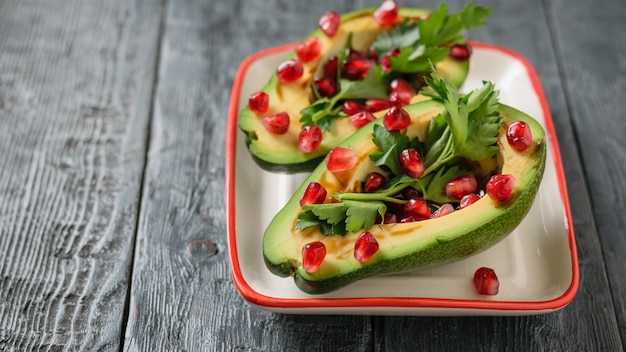 Avocado mit Granatapfelkernen, Balsamico-Sauce und Zitrone auf der weißen und roten Schüssel. Vegetarische Küche zur Gewichtsreduktion.