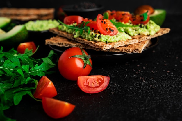 Avocado-Sandwich mit Avocado-Creme und Roggen-Knäckebrot als Snack. Ballaststoffe, Fitness und Diätkost. Roggenbrot mit Guacamole, Arugula und Kirschtomaten auf dunklem Hintergrund. Foto in hoher Qualität