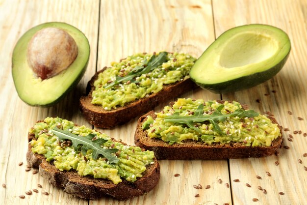 Avocado- und Rucola-Sandwiches und andere Zutaten auf einem natürlichen Holztisch.