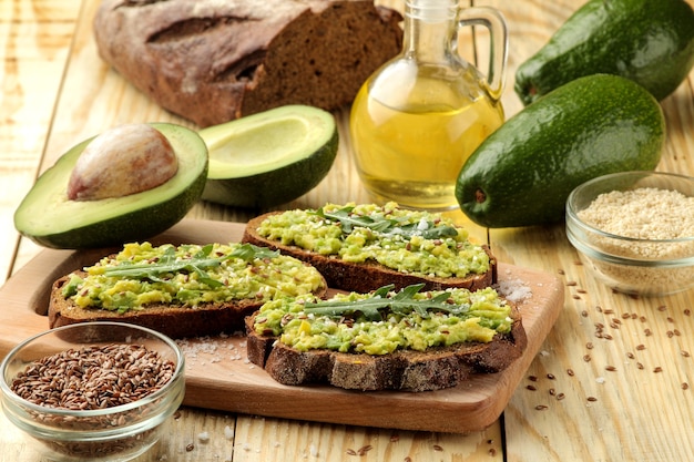 Avocado- und Rucola-Sandwiches und andere Zutaten auf einem natürlichen Holztisch.