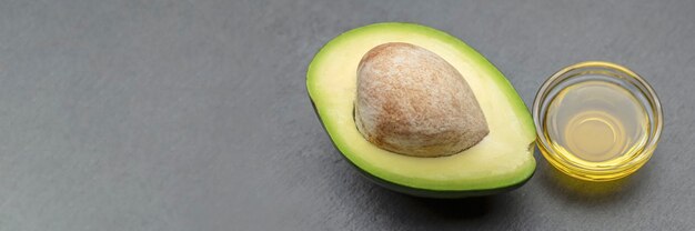 Avocadoöl. Auf einem Steintablett liegt eine Avocado mit Knochen. Avocadoöl wird in einen Teller gegossen. Banner für Druck, Etikettendesign, gesunde Ernährung.