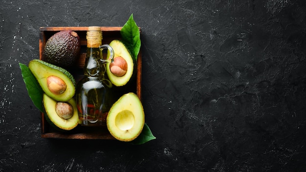 Avocadoöl und frische Avocados auf schwarzem Hintergrund Rustikaler Stil Draufsicht Freier Platz für Ihren Text