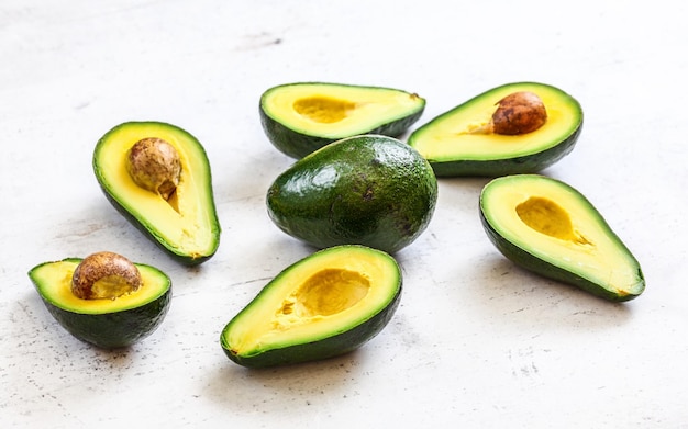 Avocados halbiert, eine ganze Birne in der Mitte, auf weißem Arbeitsbrett.