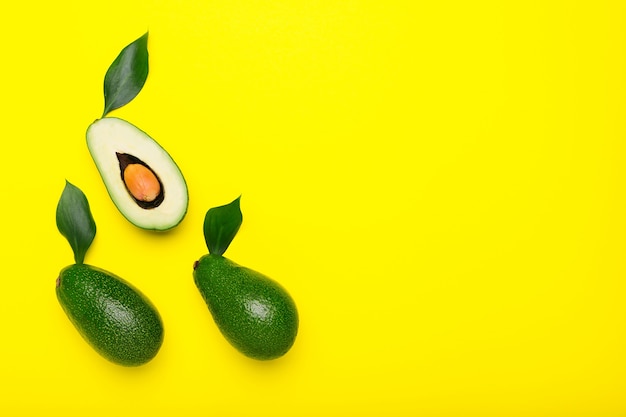 Avocados und Hälften mit Blatt auf gelbem Draufsicht-Sommerlebensmittelkonzept der Farbe