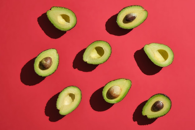 Avocados von oben auf rotem Hintergrund mit hartem Seitenlicht zeigen nach oben, einige mit Grube und andere nicht