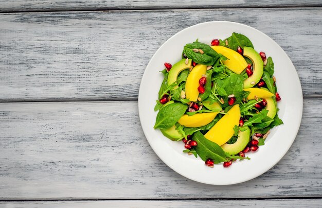 Avocadosalat mit Spinat und Granatapfel auf einem weißen Teller auf einem Holztisch