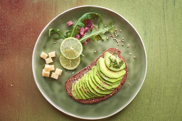 Avocadosandwich und grüner Salat mit Schinkenwürfeln auf braun-grünem strukturiertem