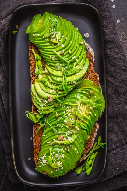 Avocadostoast mit Roggenbrot und Samen auf Schwarzblech, dunkler Hintergrund, Draufsicht.