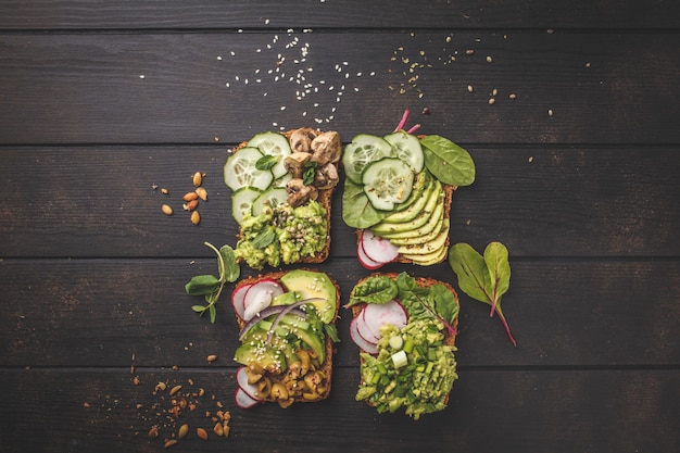 Foto avocadostoast mit verschiedenen belägen, draufsicht, dunkler hölzerner hintergrund, kopienraum.