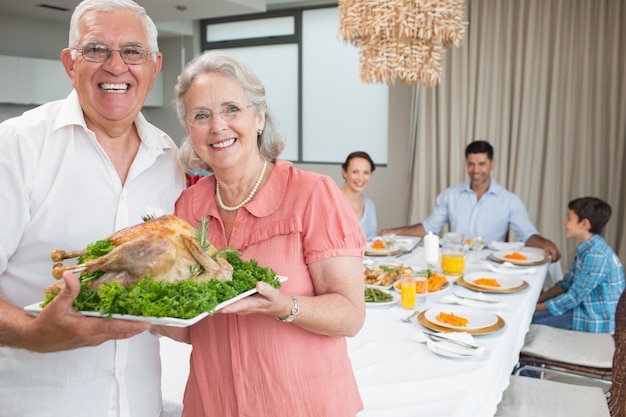 Avós segurando frango assado com a família na mesa de jantar