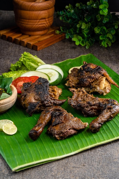 Ayam Bakar oder Brathähnchen auf Bananenblatttrieb auf rustikalem Holzhintergrund