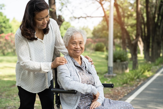 Ayuda y cuidado del cuidador Paciente asiática mayor o anciana anciana sentada y feliz en silla de ruedas en el parque sano concepto médico fuerte