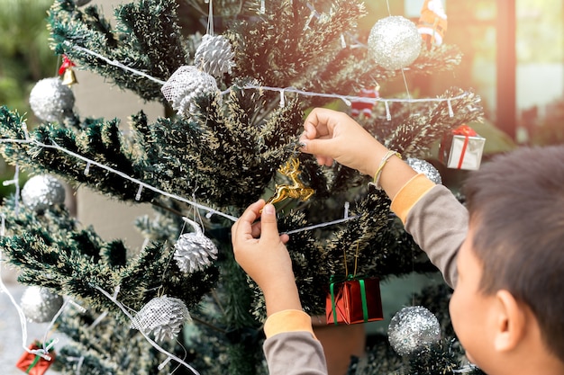 La ayuda del niño pequeño adorna el árbol de navidad con la decoración de la Navidad.